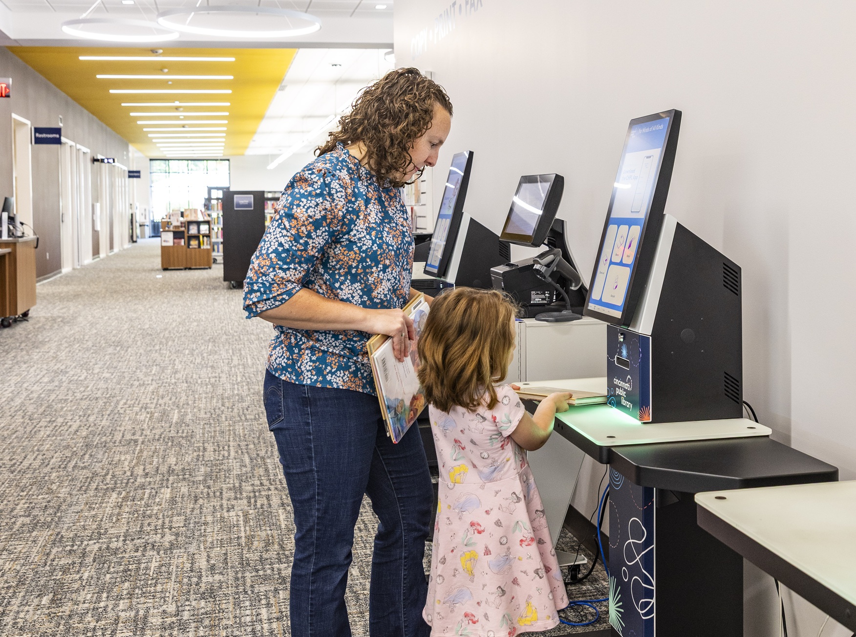 A parent and child use an RFID self-checkout kiosk at the Symmes Branch of Cincinnati Public Library.