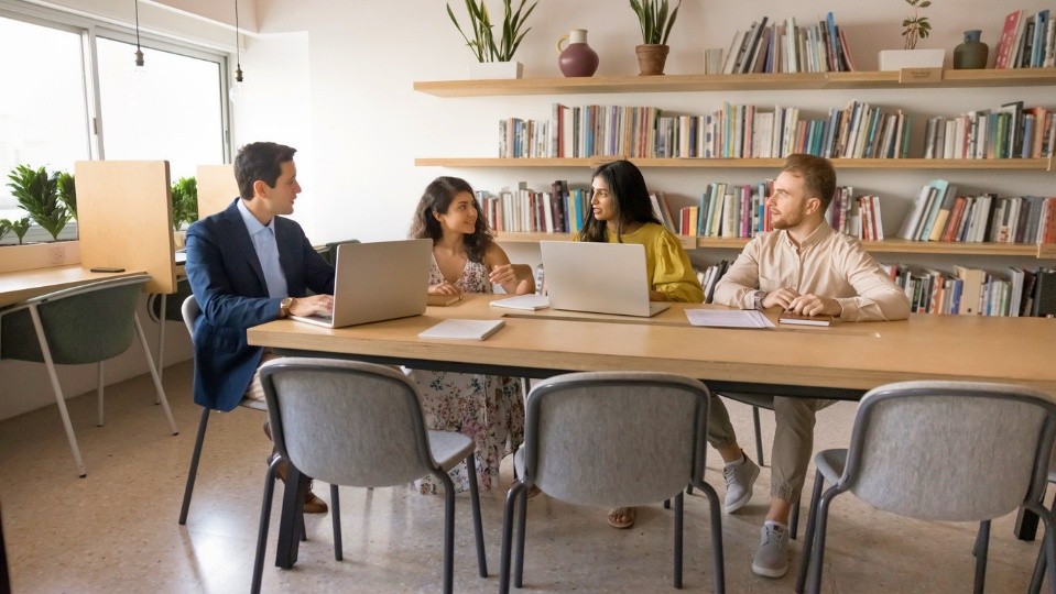 Four people meeting around a table with laptops in a library.