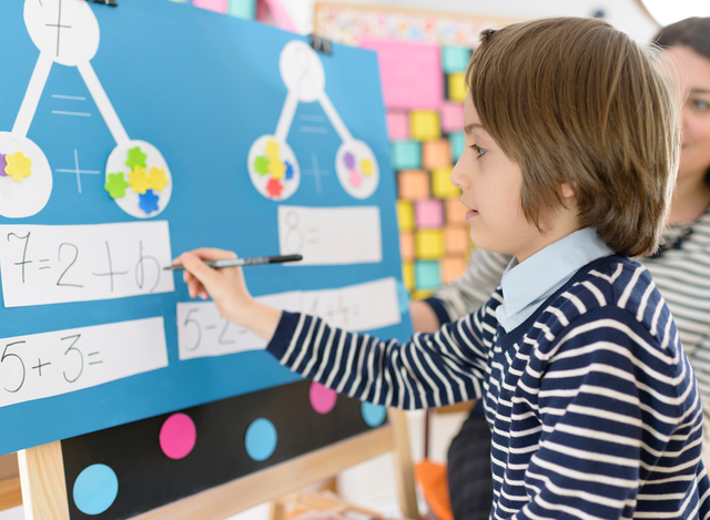 Boy does math on the board in his kindergarten classroom