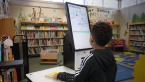 Criança utilizando totem de autoatendimento em biblioteca escolar com tecnologia Bibliotheca