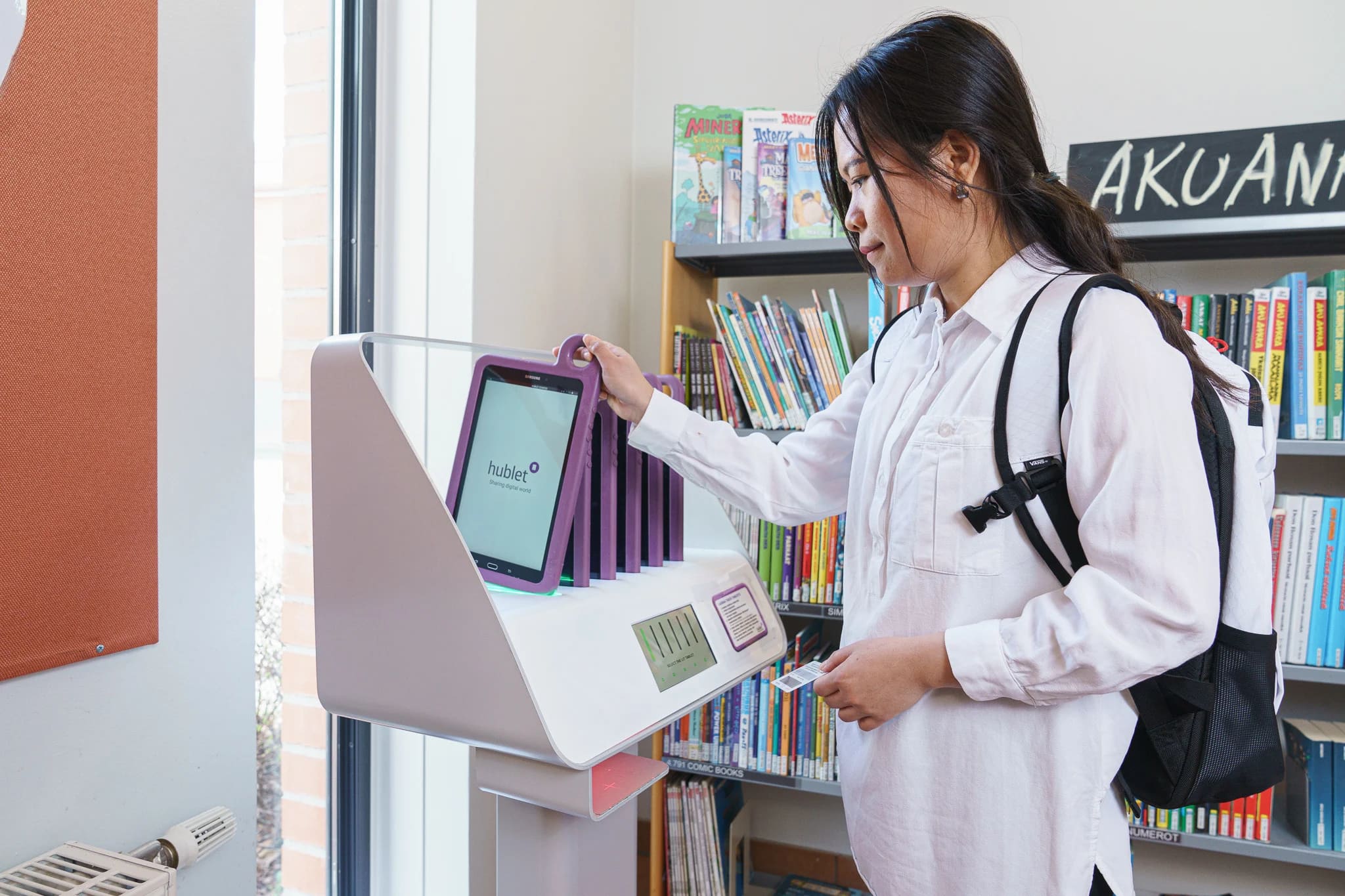 Pessoa utilizando um Hublet para empréstimo de tablet em biblioteca, promovendo autoatendimento e acesso à tecnologia para os usuários.