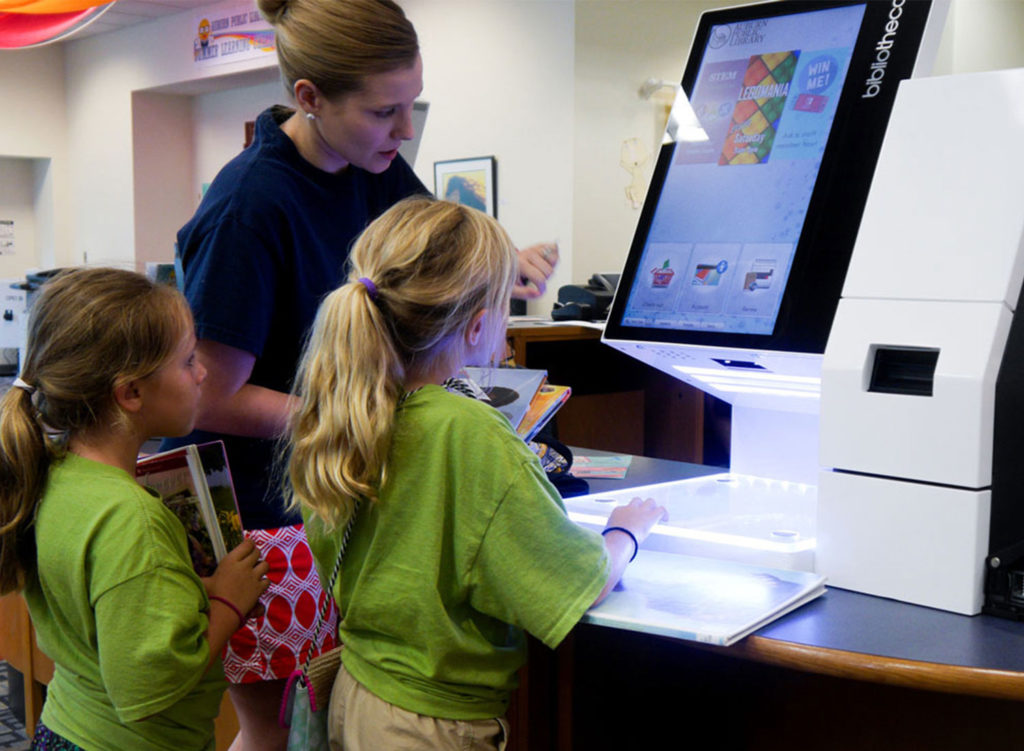Lady and 2 girls using the selfcheck 1000D to checkout some books
