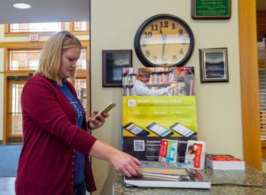 Vrouw in de Sioux Center Library checkt boek uit met haar mobiele telefoon