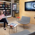 Frau sieht in einer Bibliothek auf einen digitalen Bildschirm