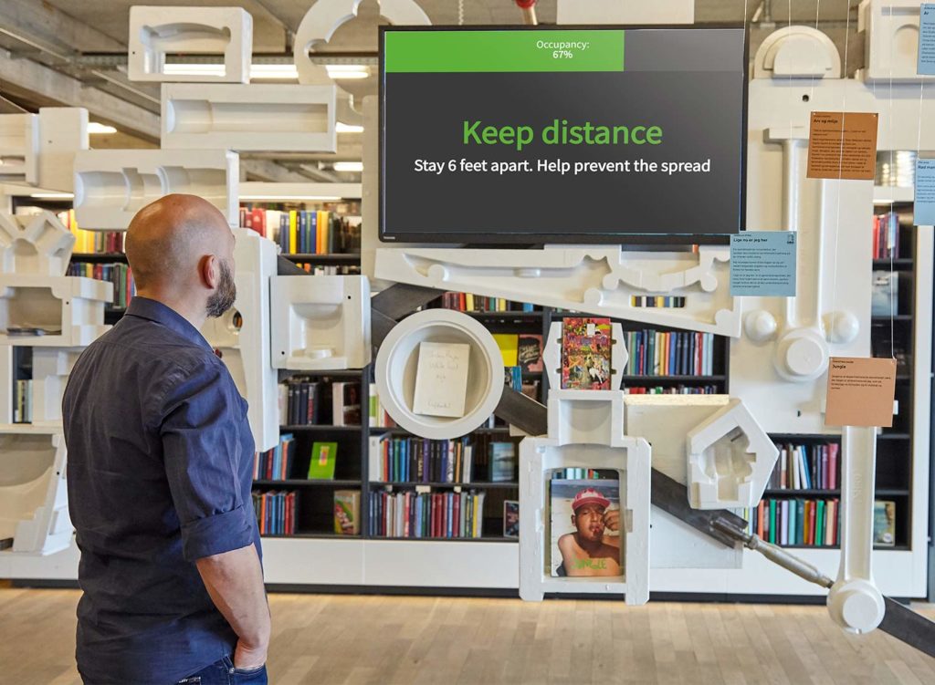 Man in bibliotheek bekijkt uniFi+ scherm met bezettingsgraad