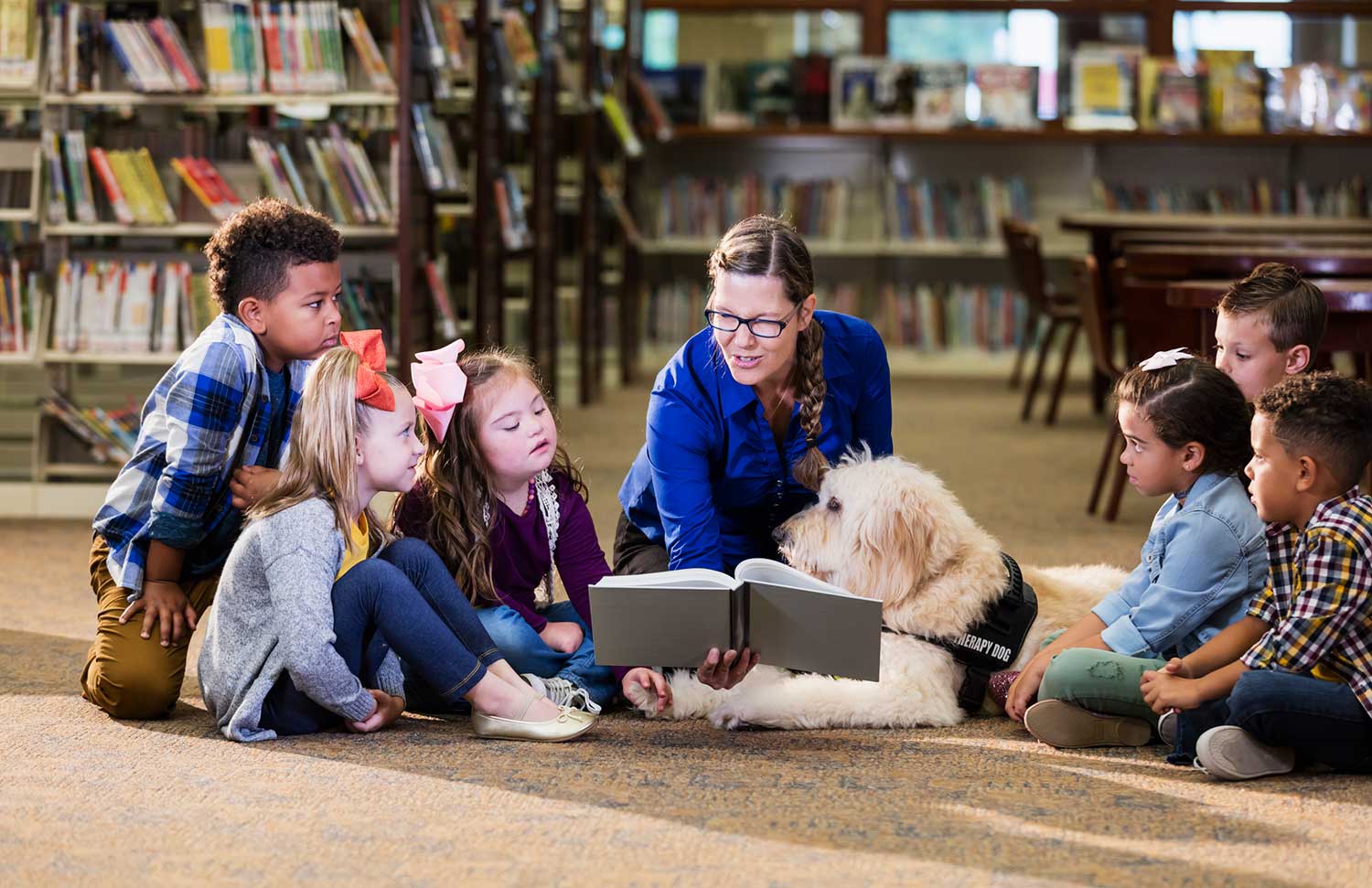 children in a library with assisted learning dog and teacher