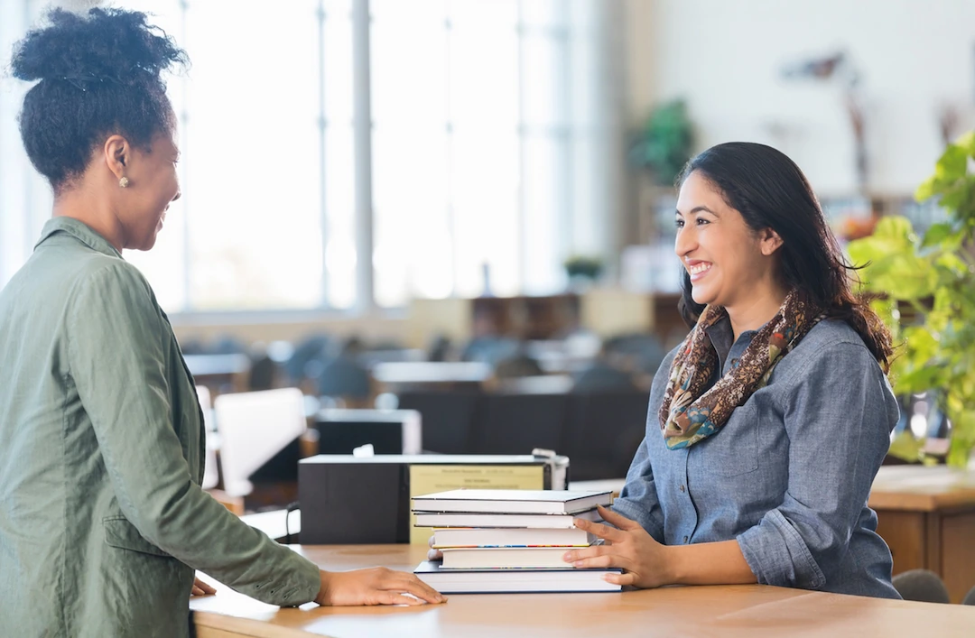 Library staff member helping a patron with a stack of books at the circulation desk
