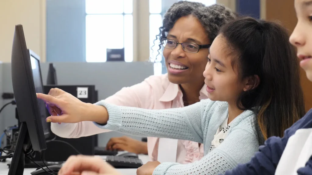 Librarian helping a young student navigate a computer at a library workstation