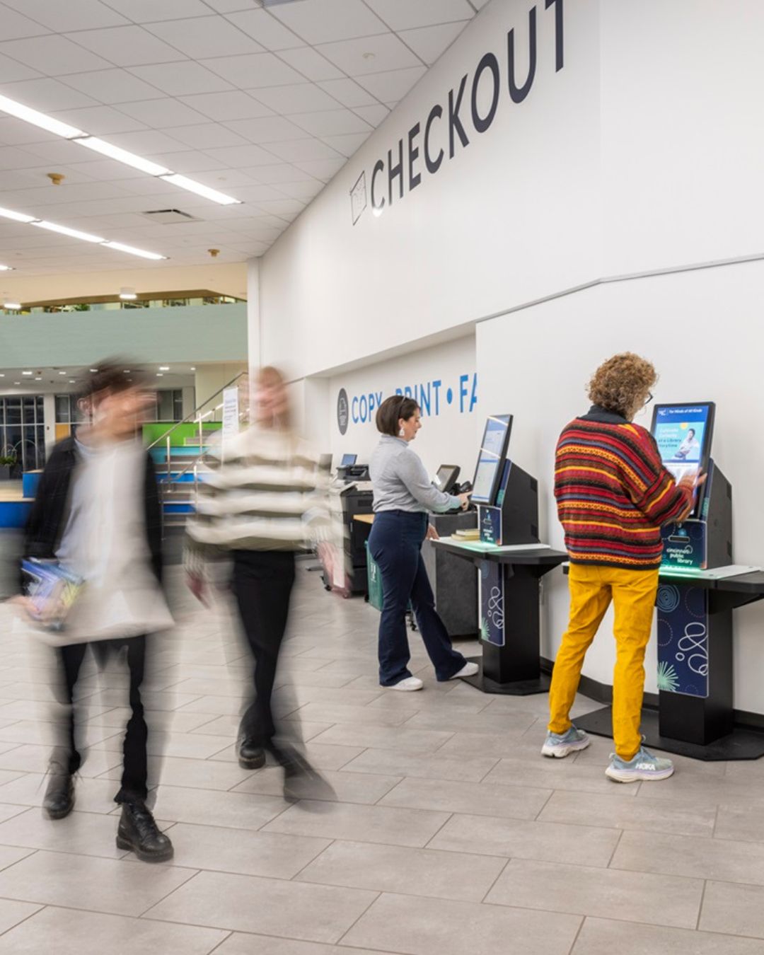 Library patrons using self-service checkout kiosks to borrow materials quickly and independently.