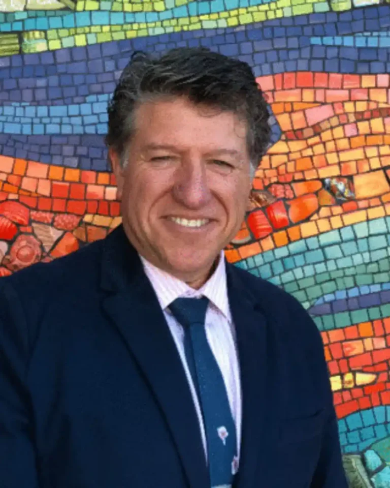Migell Acosta, director of San Diego County Library, in a dark suit in front of a colorful mosaic wall