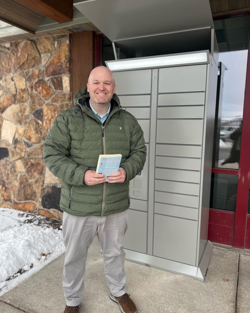 Summit County Library: Bringing the library to rural residents with remoteLocker 9 Summit County Library Director Dan Compton standing in front of the remoteLocker unit, smiling and holding a book on a snowy day